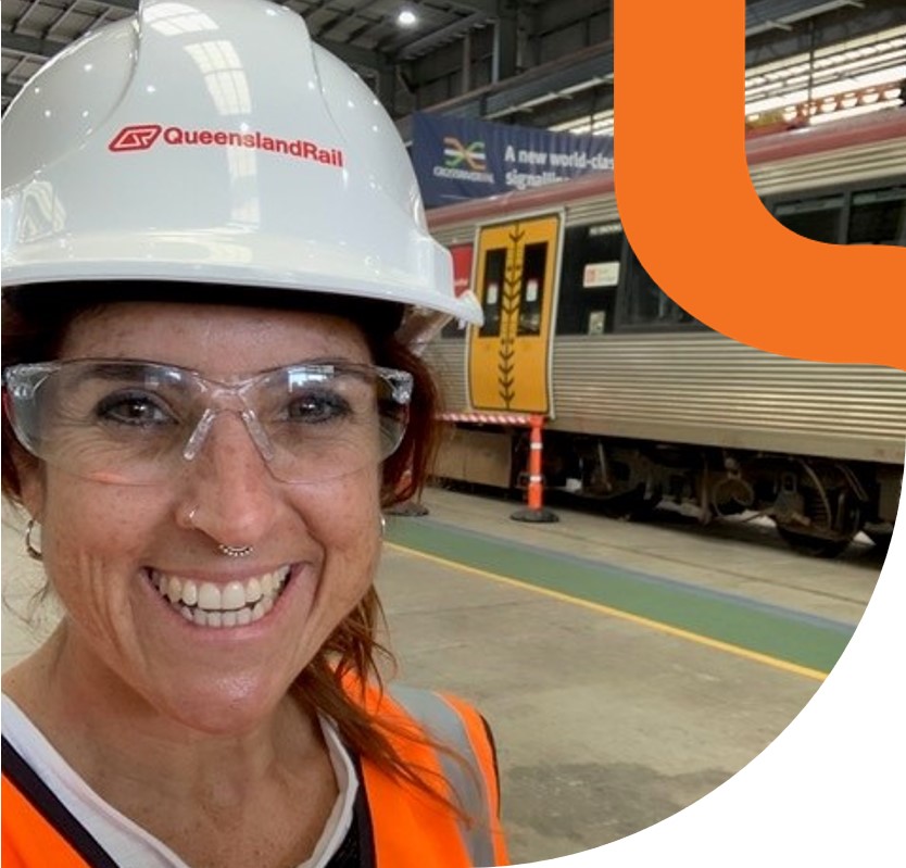 Systems Engineer wearing hard hat and nose ring standing in front of train on rail platform.