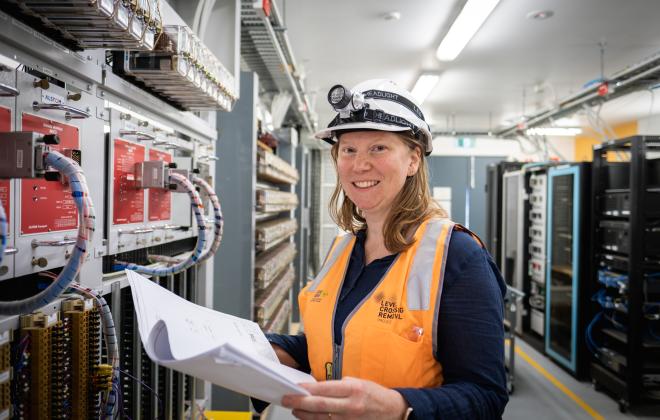 Female worker in hard hat looking at plans in front of electrical board