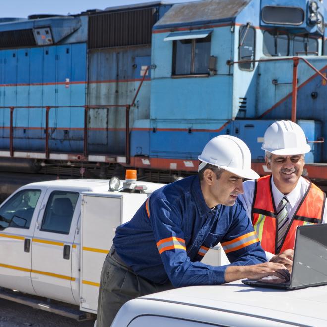 Civil Engineering Technician working on laptop with worker next to freight train