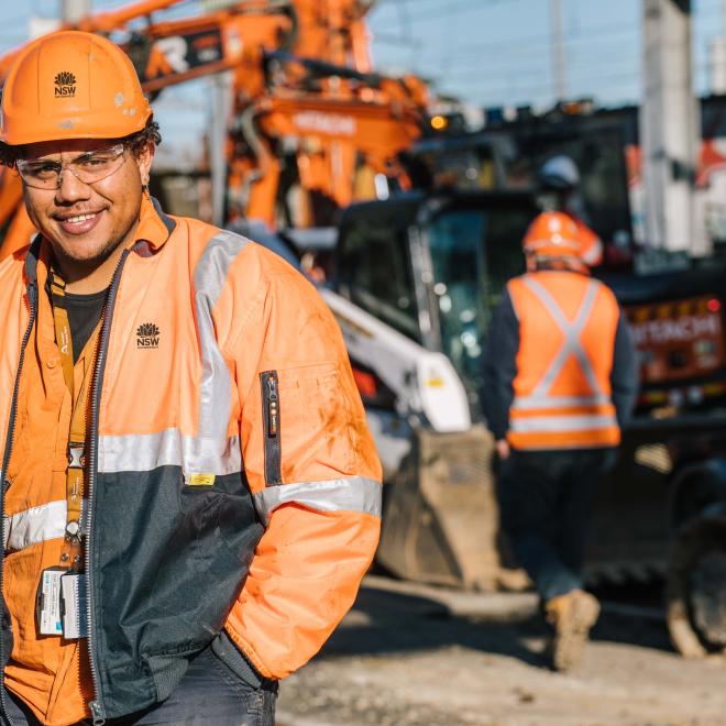 Man in hard hat and high visibility clothing with work team behind him.