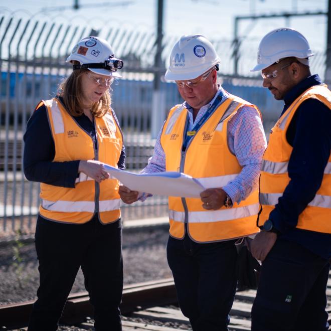 Rail Safety Officer speaking to two rail workers by the side of a track near a level crossing