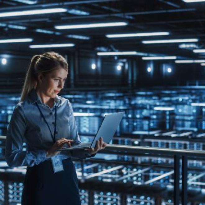 Female ICT security specialist checking her laptop in a room of compuer systems
