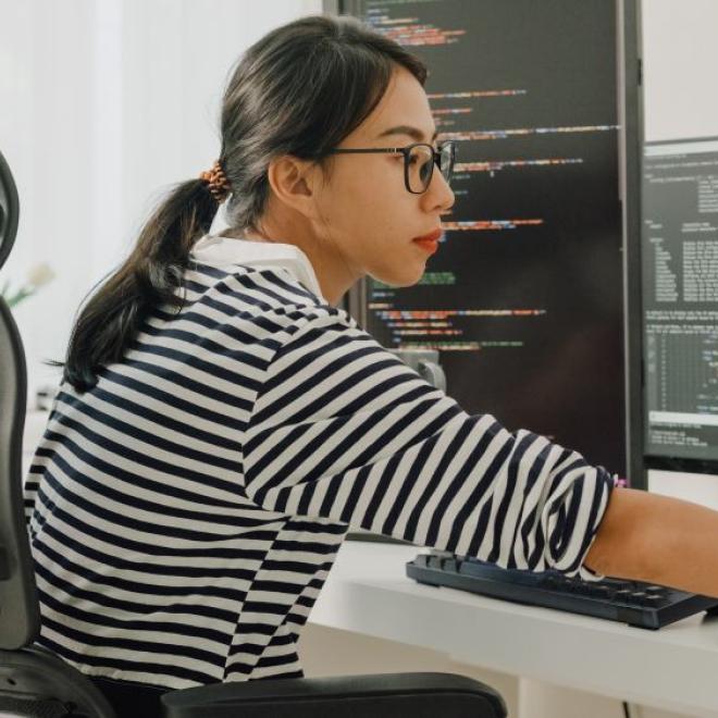 Woman in front of multiple computer screens working intently